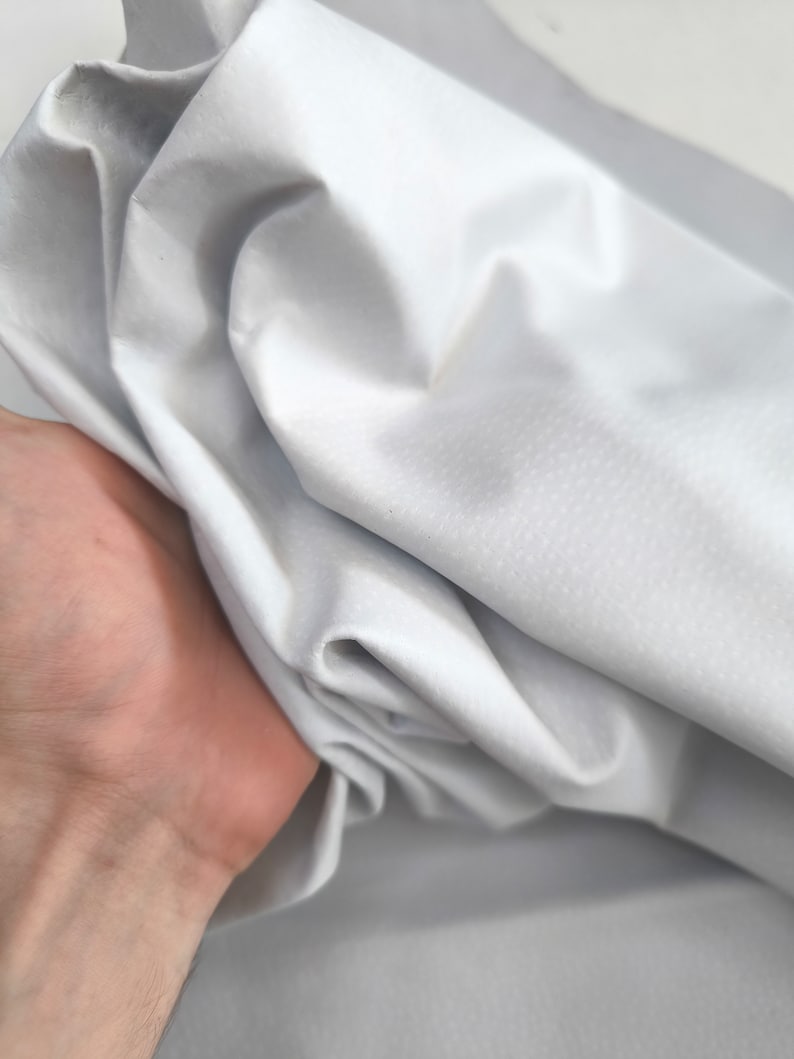 K&ouml;nnte beinhalten: Ein wei&szlig;er Stoff mit einer glatten, leicht strukturierten Oberfl&auml;che. Der Stoff ist gefaltet und zerknittert und zeigt seinen Fall und seine Flexibilit&auml;t.