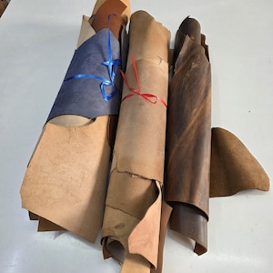 Puede incluir: Una colección de pieles de cuero enrolladas en varios colores, incluyendo beige, azul y marrón. Las pieles están atadas con cintas, mostrando las diferentes texturas y tonos del material. La imagen resalta las variaciones naturales del cuero.
