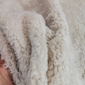 May include: Close-up of a soft, white faux fur fabric with a slightly textured surface.