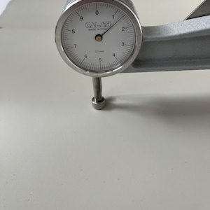 Puede incluir: Un medidor de dial plateado con una cara blanca y marcas negras. El medidor lee 0,1 mm y est&aacute; etiquetado como "CALATI MADE IN ITALY".