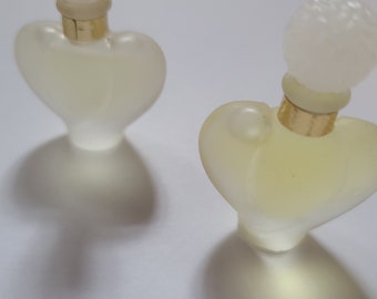 May include: Two heart-shaped glass perfume bottles with white tops and gold accents. The bottles are filled with a clear liquid.