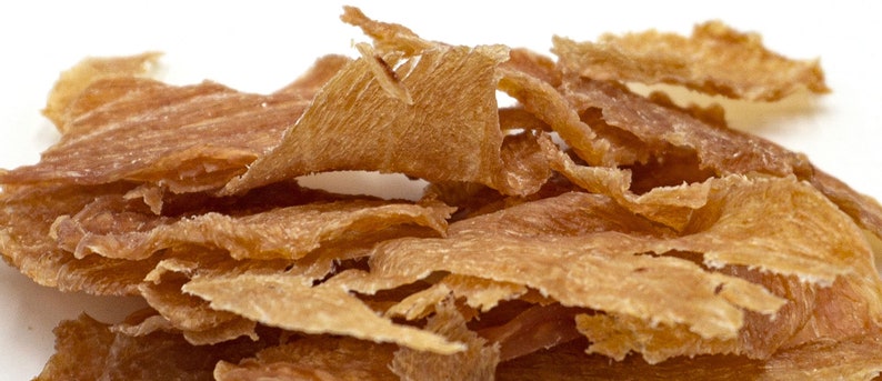 May include: A pile of thin, crispy, light brown chicken jerky strips.