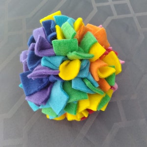 May include: A colorful felt toy for dogs, made of multiple layers of fabric in rainbow colors, including blue, green, yellow, orange, and red.