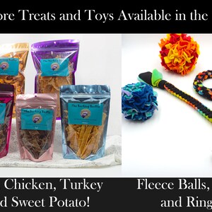 May include: Assortment of dog treats in clear plastic bags with the text "The Barking Beddie" on the front. The bags contain beef, chicken, turkey, and sweet potato treats.  On the right side of the image, there are three dog toys: a multi-colored fleece ball, a multi-colored rope tug toy, and a black and white rope ring toy.
