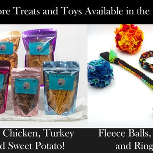 May include: Assortment of dog treats in clear plastic bags with the text "The Barking Beddie" on the front. The bags contain beef, chicken, turkey, and sweet potato treats.  On the right side of the image, there are three dog toys: a multi-colored fleece ball, a multi-colored rope tug toy, and a black and white rope ring toy.