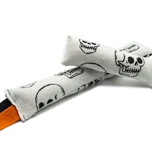 May include: Two white fabric dog toys with black skull designs and orange and black fabric tails.