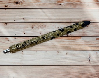 May include: Gold glitter pen with a black leopard print design and the name "Ashley" written on it.