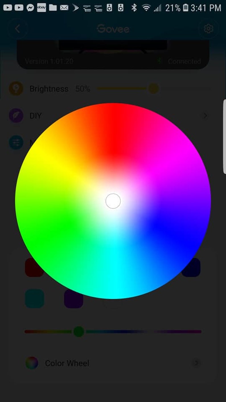 May include: A smartphone screen displaying a color wheel with a slider below it. The color wheel is a circular gradient of colors from red to orange, yellow, green, blue, indigo, and violet. The slider is a horizontal bar with a green dot in the middle. The text "Color Wheel" is below the slider. The text "Brightness: 50%" is above the color wheel.