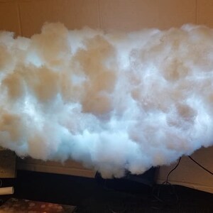 May include: A white cloud-shaped lamp with a white light shining through it. The lamp is made of cotton and is sitting on a black base.