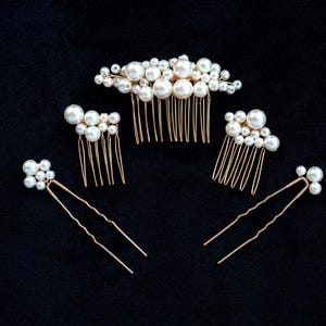 May include: A collection of bridal hair accessories on a black background. The set includes a large comb, two smaller combs, and two hair pins, all adorned with faux pearls. The metal components are gold-toned, creating a classic and elegant look.
