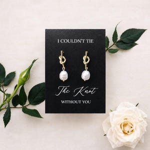 May include: Gold-colored knot earrings with white pearl drops displayed on a black card. The card reads "I COULDN'T TIE The Knot WITHOUT YOU" in elegant script. The image is set against a soft, neutral background with floral accents.