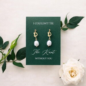 May include: Gold-tone knot earrings with white pearl drops displayed on a dark green card. The card reads "I COULDN'T TIE The Knot WITHOUT YOU". A white rose and green leaves are in the background.