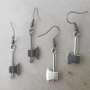 Puede incluir: Tres pares de pendientes de hacha plateados. Cada pendiente tiene un pequeño dije de hacha con un diseño detallado.