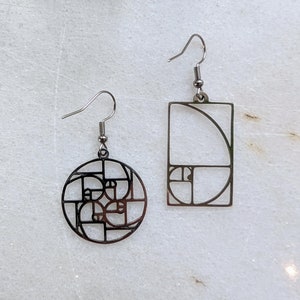Könnte beinhalten: Ein Paar silberne Ohrringe mit einem geometrischen Design, das von der Fibonacci-Sequenz inspiriert ist. Ein Ohrring ist ein Kreis, der andere ein Rechteck.