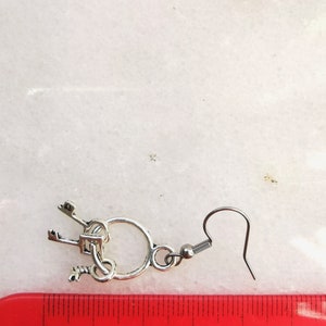 May include: Silver key earrings with a circle charm and a hook closure. The earrings are approximately 2 inches long.