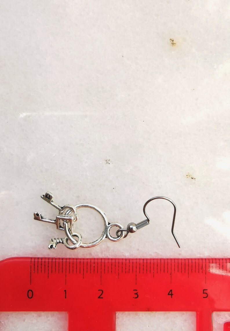 May include: Silver key earrings with a circle charm and a hook closure. The earrings are approximately 2 inches long.