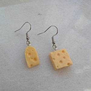 Könnte beinhalten: Ein Paar silberne Ohrringe mit einem gelben Käse-Anhänger. Der Käse-Anhänger hat Löcher.