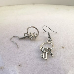 May include: Silver key earrings with a circle charm and a dangling key charm. The earrings have a hook closure.