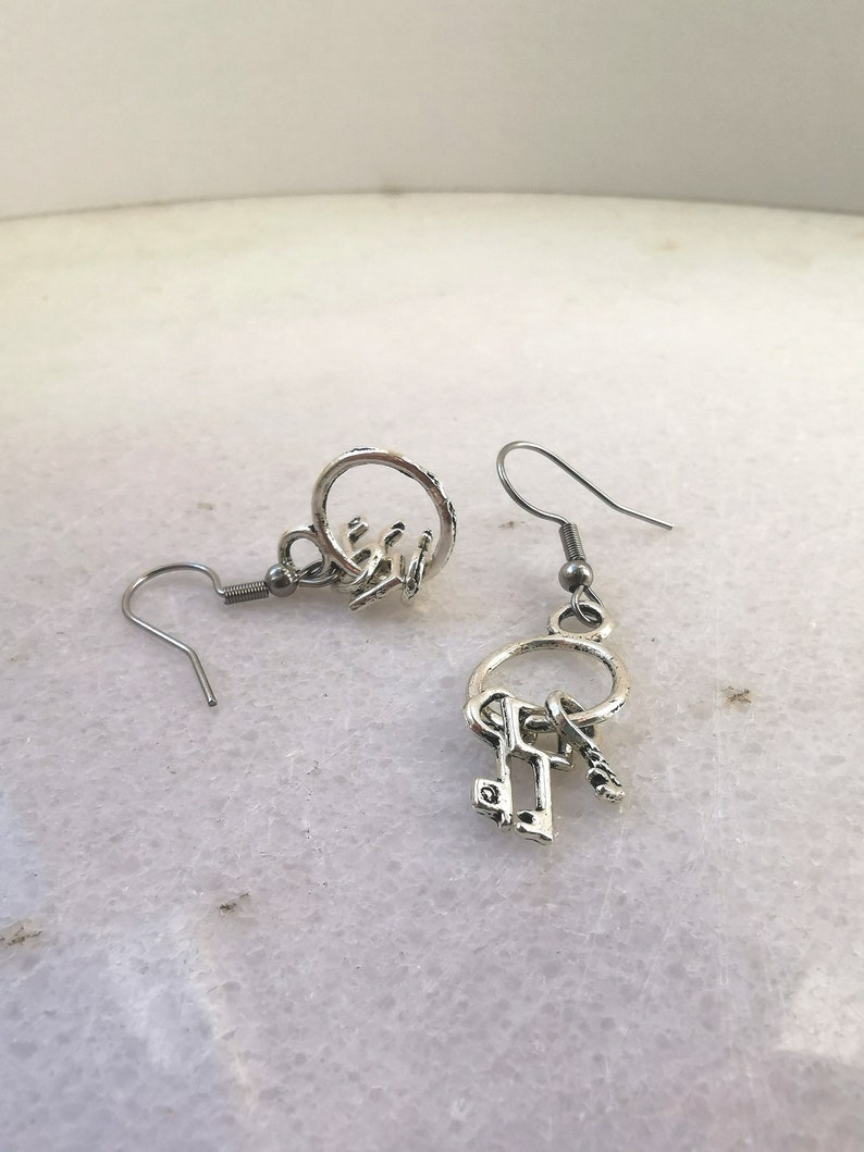 May include: Silver key earrings with a circle charm and a dangling key charm. The earrings have a hook closure.