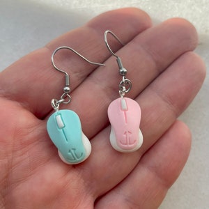 May include: A pair of silver dangle earrings with a pink and a light blue computer mouse charm. The mouse charms have a white bottom and a silver anchor symbol.