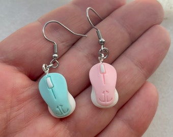 Op de afbeelding: Een paar zilveren oorhangers met een roze en een lichtblauwe computermuis charme. De muis charmes hebben een witte onderkant en een zilveren anker symbool.