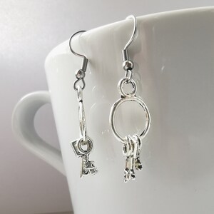 May include: A pair of silver key-shaped earrings. One earring features a single key charm, while the other has a cluster of three keys hanging from a hoop.