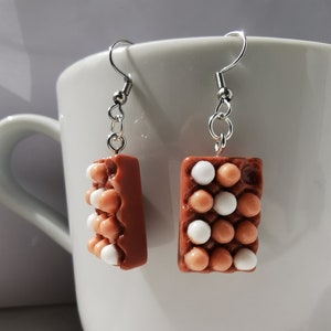 Peut inclure: Une paire de boucles d'oreilles pendantes avec un motif de bo&icirc;te &agrave; &oelig;ufs marron avec des &oelig;ufs blancs et marrons. Les boucles d'oreilles sont en p&acirc;te polym&egrave;re et ont des crochets argent&eacute;s.