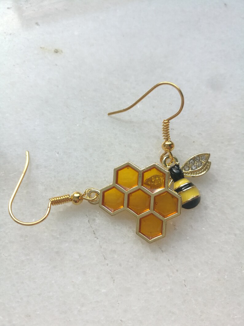K&ouml;nnte beinhalten: Goldene Bienen- und Wabenohrringe. Die Biene hat schwarze und gelbe Streifen und klare Strasssteine. Die Wabe ist hellbernsteinfarben.
