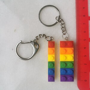 May include: A rainbow-colored keychain made of stacked Lego bricks. The keychain is attached to a silver chain and two silver rings.