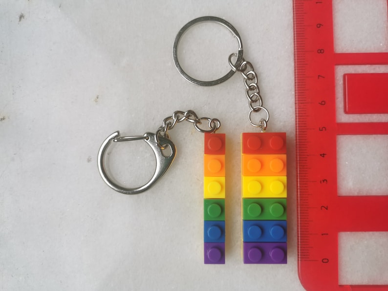 May include: A rainbow-colored keychain made of stacked Lego bricks. The keychain is attached to a silver chain and two silver rings.