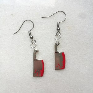 Puede incluir: Un par de pendientes de plata con detalles rojos en forma de cuchillo de carnicero.