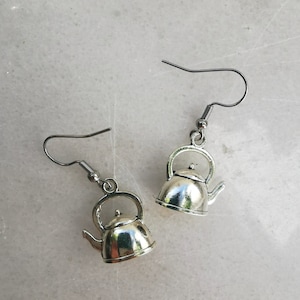 Puede incluir: Un par de pendientes de plata con forma de tetera. Las teteras tienen un diseño clásico con un pico y un asa.