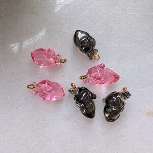 May include: Six heart-shaped charms, three pink and three black, with gold jump rings. The charms are made of glass and have a slightly textured surface.
