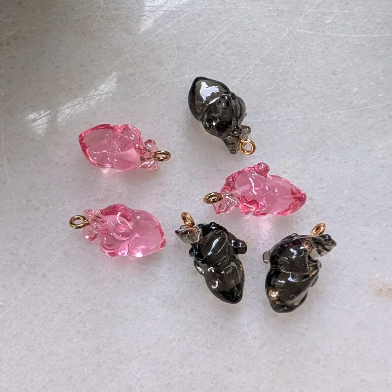 May include: Six heart-shaped charms, three pink and three black, with gold jump rings. The charms are made of glass and have a slightly textured surface.
