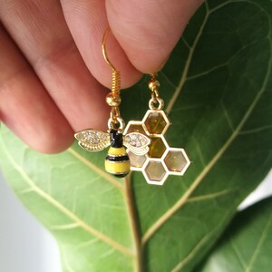 K&ouml;nnte beinhalten: Goldene Bienen- und Wabenohrringe. Die Biene ist schwarz und gelb mit klaren Strasssteinen. Die Wabe ist golden mit klaren Strasssteinen.