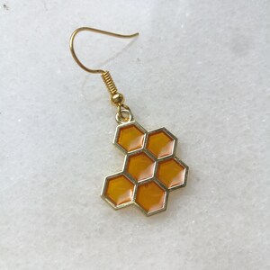 K&ouml;nnte beinhalten: Goldener Honigwaben-Ohrring mit gelber Emaille-Oberfl&auml;che. Der Ohrring ist im H&auml;nge-Stil mit einem Hakenverschluss.
