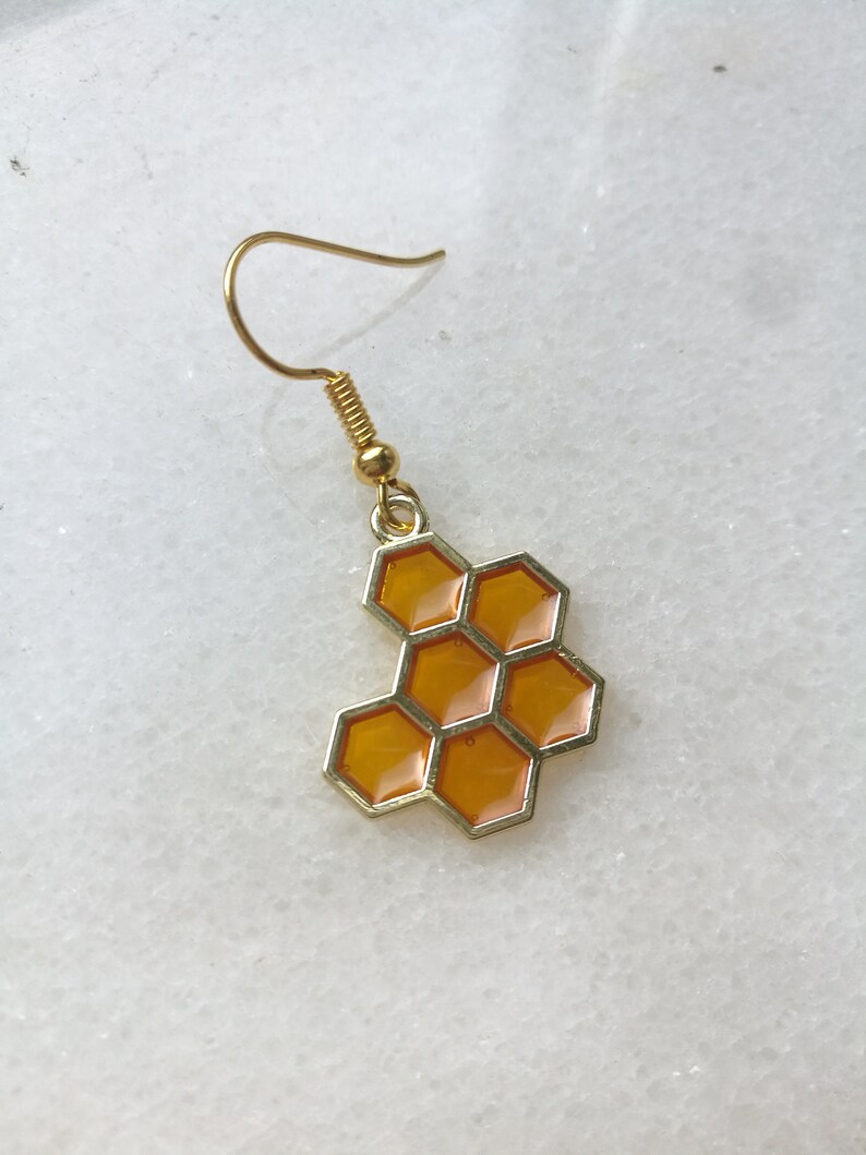 K&ouml;nnte beinhalten: Goldener Honigwaben-Ohrring mit gelber Emaille-Oberfl&auml;che. Der Ohrring ist im H&auml;nge-Stil mit einem Hakenverschluss.