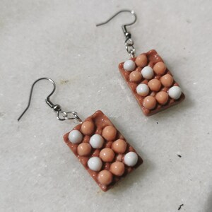 Peut inclure: Une paire de boucles d'oreilles en forme de bo&icirc;tes &agrave; &oelig;ufs avec des &oelig;ufs bruns et blancs. Les boucles d'oreilles sont en p&acirc;te polym&egrave;re et ont des crochets argent&eacute;s.