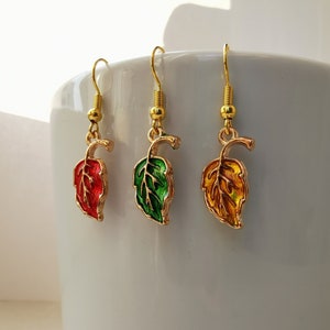 May include: Three leaf-shaped earrings with gold-coloured hooks. Each leaf is a different colour: red, green, and yellow-orange. The earrings are hanging against a white background, showcasing the vibrant colours and intricate details of the jewellery.
