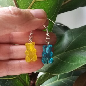 K&ouml;nnte beinhalten: Ein Paar Gummib&auml;rchen-Ohrringe, einer gelb und einer blau, die an silbernen Haken h&auml;ngen.