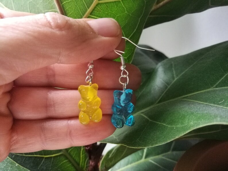 K&ouml;nnte beinhalten: Ein Paar Gummib&auml;rchen-Ohrringe, einer gelb und einer blau, die an silbernen Haken h&auml;ngen.