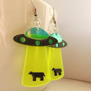 May include: A pair of neon green and black UFO earrings with a black cow silhouette on each earring.