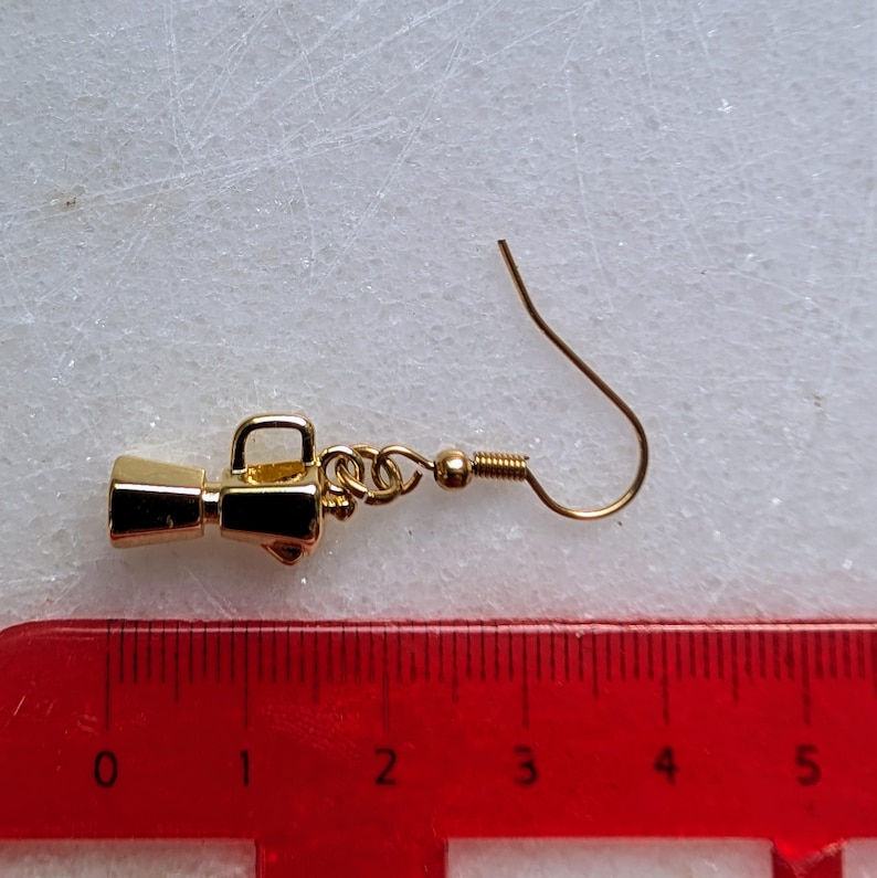 May include: A gold-colored earring shaped like a megaphone. The earring has a small handle and a hook for the ear. The megaphone is approximately 1 inch long.
