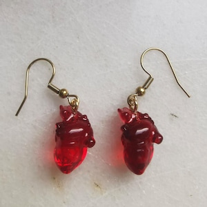 May include: A pair of red heart-shaped dangle earrings with gold hooks.