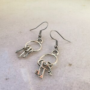 May include: A pair of silver earrings with a circle charm and three small key charms dangling from each earring.