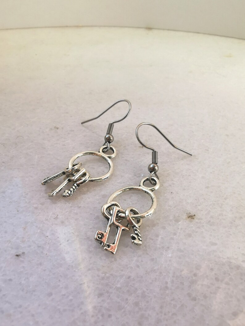 May include: A pair of silver earrings with a circle charm and three small key charms dangling from each earring.