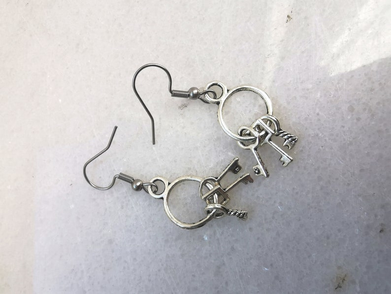May include: Silver key earrings with a circle design and multiple keys dangling from the bottom.