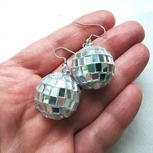 May include: A pair of silver disco ball earrings. Each earring is a small, round, mirrored ball with a silver hook.
