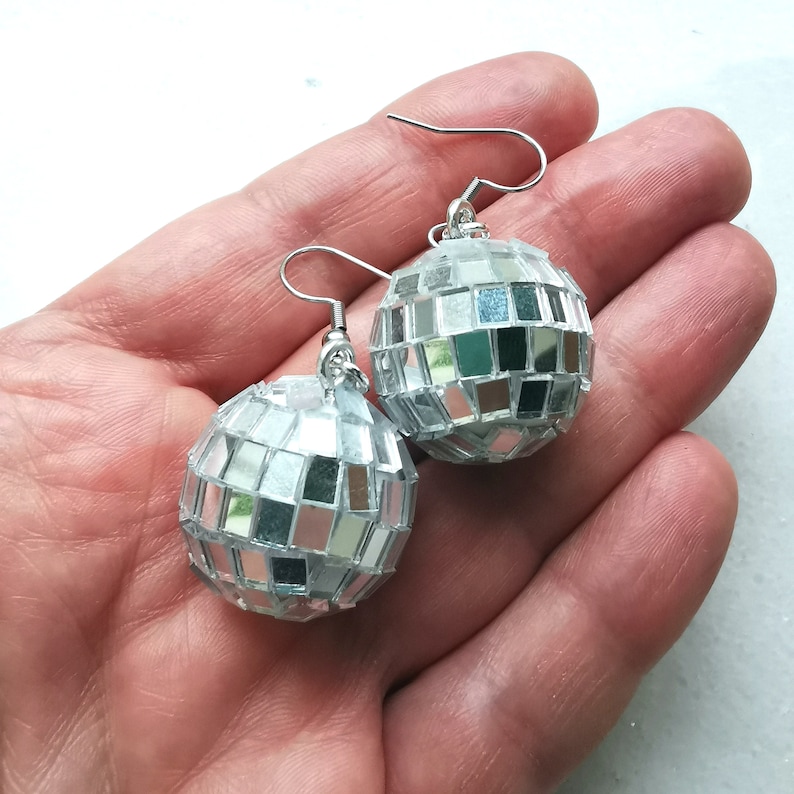 May include: A pair of silver disco ball earrings. Each earring is a small, round, mirrored ball with a silver hook.