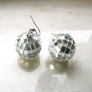 May include: A pair of silver disco ball earrings. Each earring is a small sphere covered in mirrored tiles.